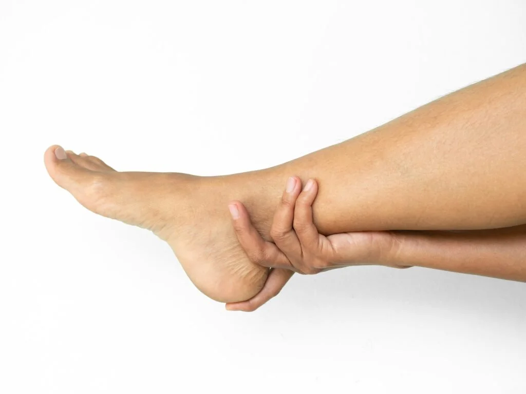 Person gripping their ankle and heel with both hands indicating pain